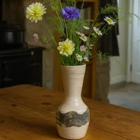 Handmade stoneware vase with British wildflowers on an oak table in a cozy country home kitchen.