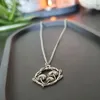 Circular pendant on silver chain depicting 3 mushrooms in a ring of leaves with a textured appearance