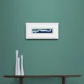 Narrow Blue White and Teal Waves Print in Framed in White on a Blue Wall Above Dark Shelf and Vase Set