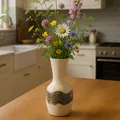 Handmade stoneware vase with British wildflowers on an oak table in a cozy country home kitchen.