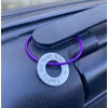 1 inch aluminium washer stamped with the words living my best life.  the washer hangs on a purple wire loop to make a luggage tag.  the item is shown attached to the handle of a suitcase