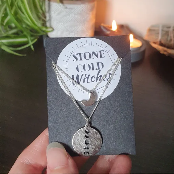 2 piece layered necklace on silver chain. circular silver coloured pendant with vertical moon phase cut out on the longer chain and a dainty shiny crescent moon on a short choker style chain