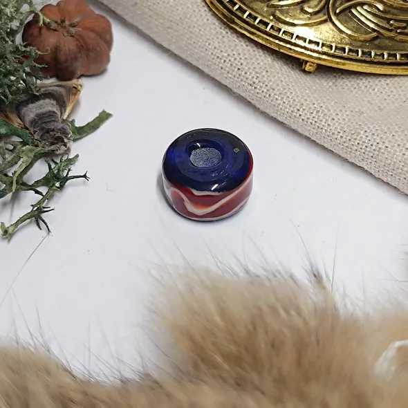 A photo of the bead on a white background but slightly framed with items associated with the viking era
