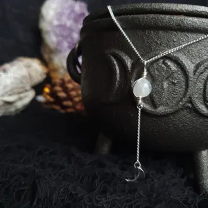Small moonstone sphere bound in a simple wire wrap onto silver chain, there is an extra loop on the moonstone wire wrap that holds another small piece of chain (approx 3cm) where a dainty shiny silver crescent moon e=pendant is attached ina  droplet formation from the moonstone. Moonstone is a bright white with delicate flashes of blue, opaque is some areas and translucent in others