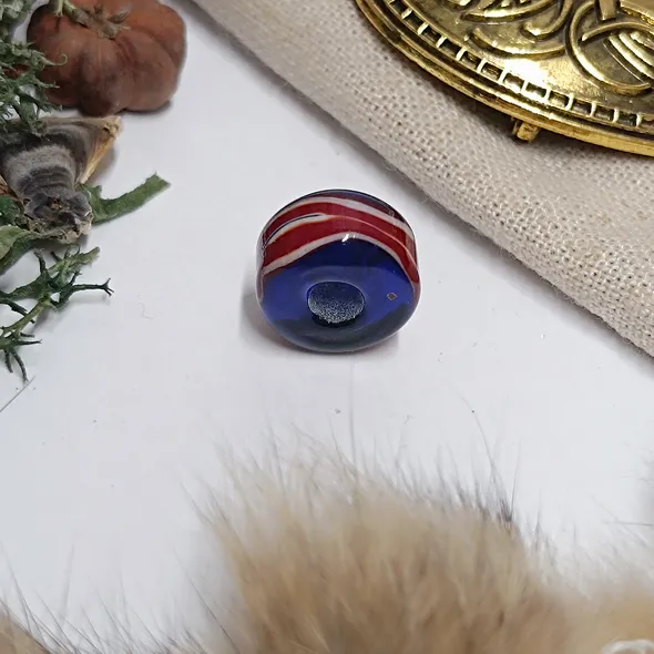 A photo of the bead on a white background but slightly framed with items associated with the viking era