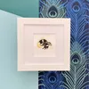 Mini Honey Bee Lino Print on Yellow Watercolour Wash Framed in White in front of Peacock Feather Paper