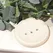 Image shows a cream coloured round soap dish with 3 drainage holes, on a cream background surrounded by eucalyptus