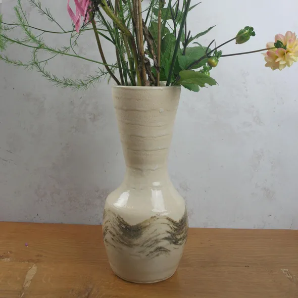 Handmade wheel-thrown stoneware vase with textured slip design, shown on a wooden table with fresh flowers.