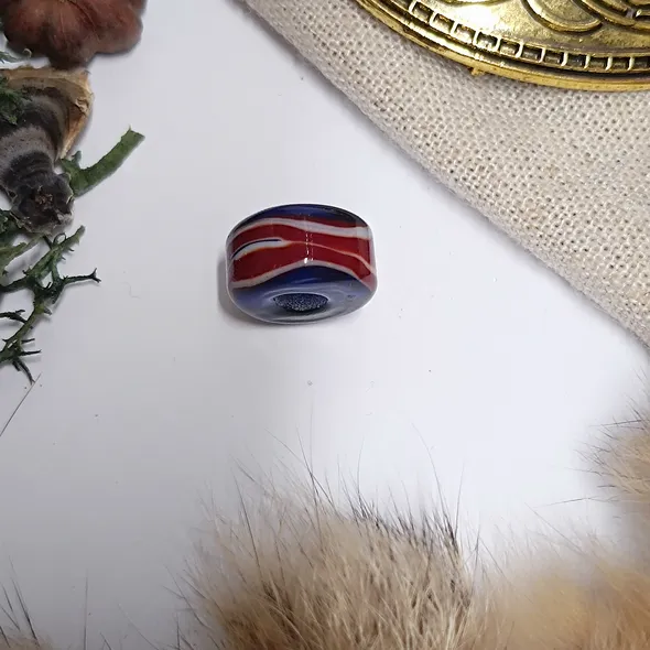 A photo of the bead on a white background but slightly framed with items associated with the viking era