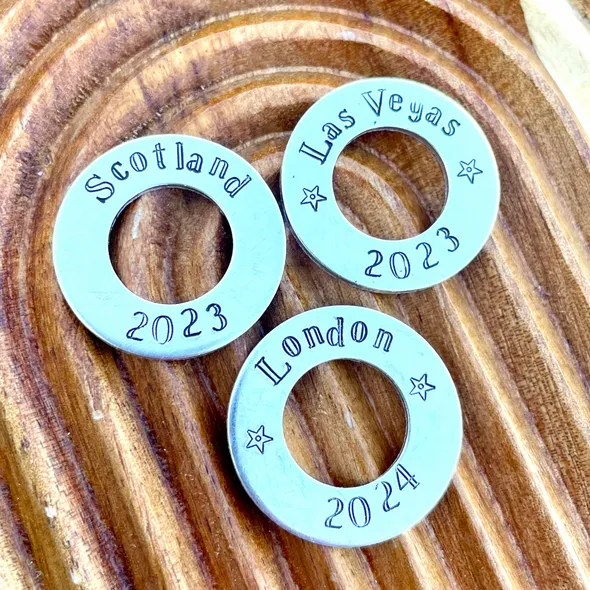 image shows 3 additional 1 inch aluminium washers which can be added to any wire luggage tag.  the washers shown are stamped with the words scotland 2023, las vegas 2023 and london 2024.  the listing is for one personalised additional washer which can be added to any wire luggage tag.
