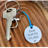 1 inch aluminium disc hand stamped with the words our happy place in capital letters with a small heart below.  shown on a royal blue cord to turn the disc into a hanging keyring