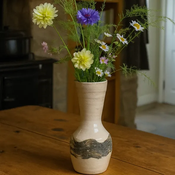 Handmade stoneware vase with British wildflowers on an oak table in a cozy country home kitchen.