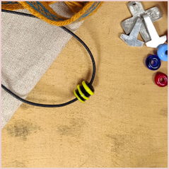 Subbersund Wasp Bead. A black bead with three raised lines of yellow shown on a cord in a flatlay