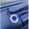 1 inch aluminium washer stamped with the words living my best life.  the washer hangs on a purple wire loop to make a luggage tag.  the item is shown attached to the handle of a suitcase