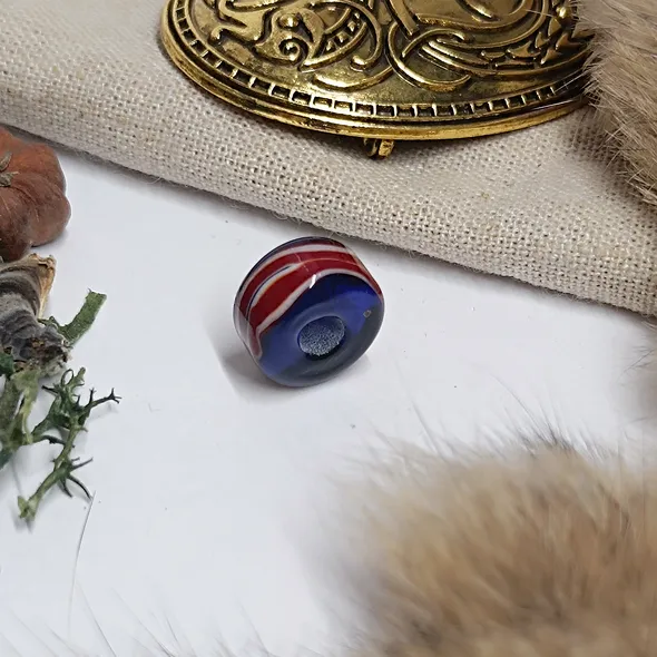 A photo of the bead on a white background but slightly framed with items associated with the viking era
