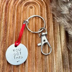 1 inch aluminium disc hand stamped with the words you got this in capital letters with an arrow design below.  shown on a red cord turning the disc into a hanging keyring
