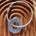 1 inch aluminium washer that can be personalised.  the image shows it stamped with the words stamped by gill est 2022.  the washer is threaded onto a silver wire loop to make a luggage tag.