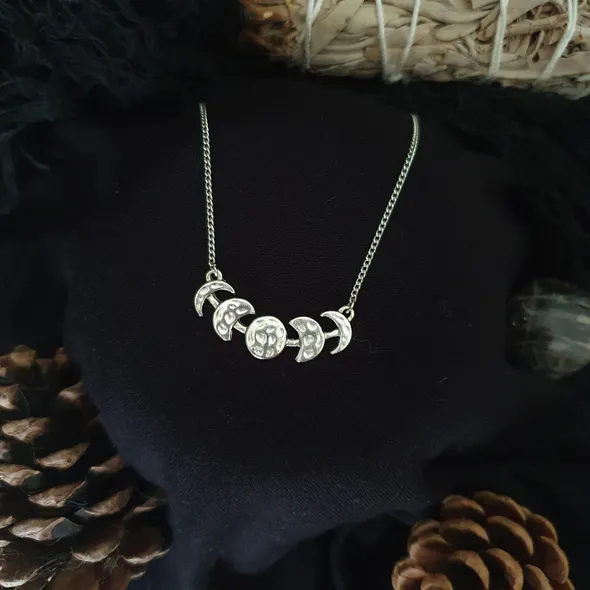 Silver colour moon phase necklace with a full moon in the middle and 2 crescent moons either side, decreasing in size. The pendant has a shiny yet textured appearance and hangs on a silver plated chain about collerbone length