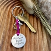 1 inch aluminium disc hand stamped with the words follow your dreams in capital letters, with small moon and stars design above.  Shown on a deep pink cord to turn the disc into a hanging keyring