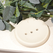 Image shows a cream coloured round soap dish with 3 drainage holes, on a cream background surrounded by eucalyptus
