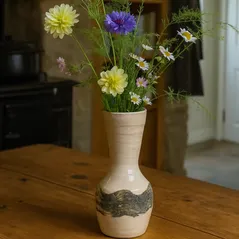 Handmade stoneware vase with British wildflowers on an oak table in a cozy country home kitchen.