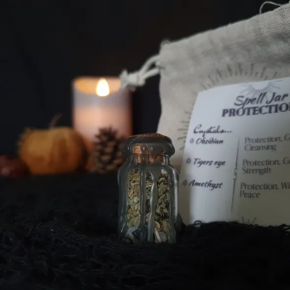 Mini spell jar for protection - jar is clear glass containing a mix of herbs and crystals, topped with a cork stopper and sealed with black wax which drips down the sides of the jar
