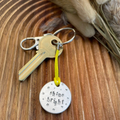1 inch aluminium disc hand stamped with the words shine bright in lower case lettering, surrounded by small stars.  Shown attached to a yellow cord turning the disc into a hanging keyring