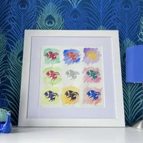 Honey Bee Rainbow Lino Print on Watercolour Washes Framed in White on a Chest of Drawers in front of Peacock Feather Paper