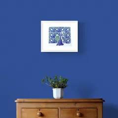 Peacock with Splayed Feathers in Green and Blue Framed in White on a Blue Wall Above a Wooden Drawer Unit