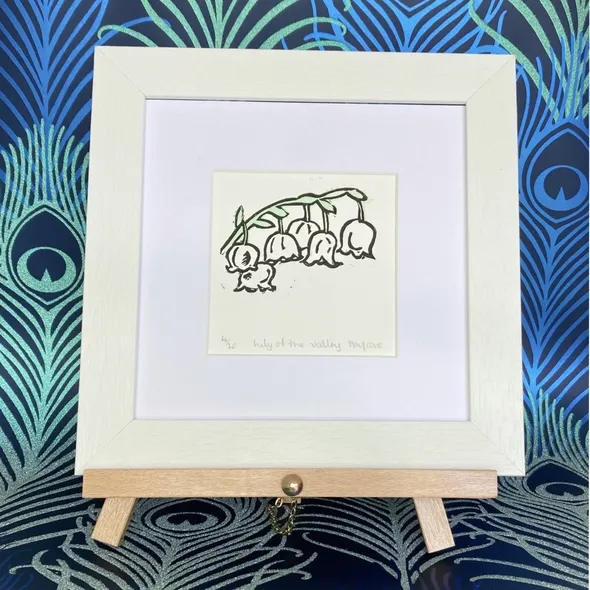Lily of the Valley framed in white on a beech easel against a peacock background