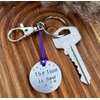 1 inch aluminium disc hand stamped with the words the time is now in lower case font, with small stars above and below.  shown on a purple cord to turn the disc into a hanging keyring