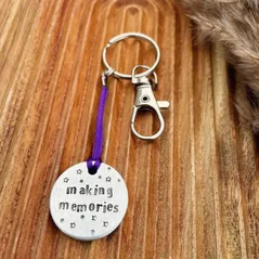 1 inch aluminium disc hand stamped with the words making memories with stars above and below.  shown on a purple cord turning the disc into a hanging keyring